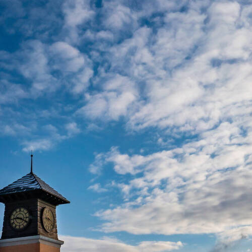A clock tower stands against a vibrant blue sky dotted with wispy white clouds.